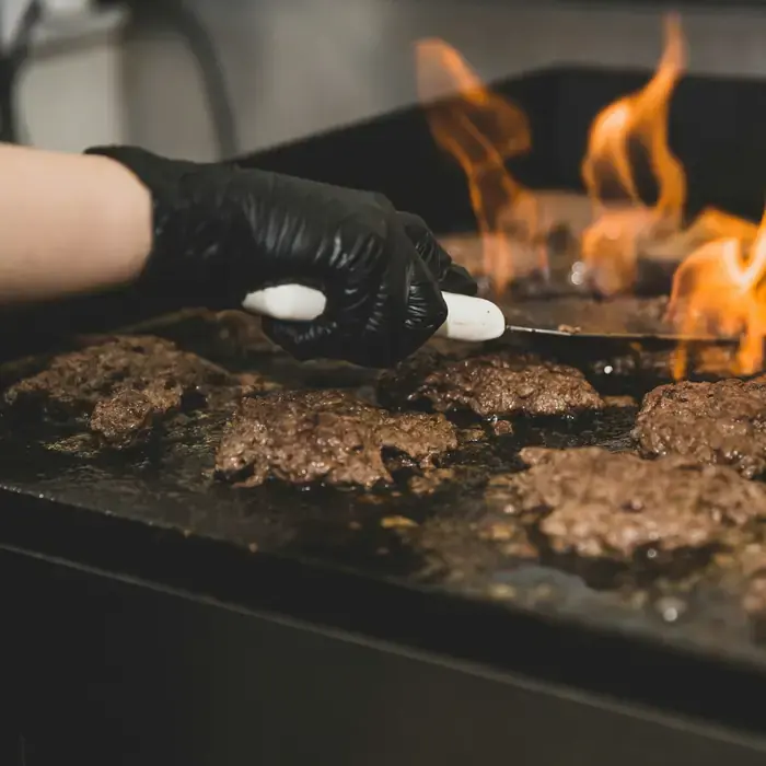 Patties searing on a flat top with flames rising behind them