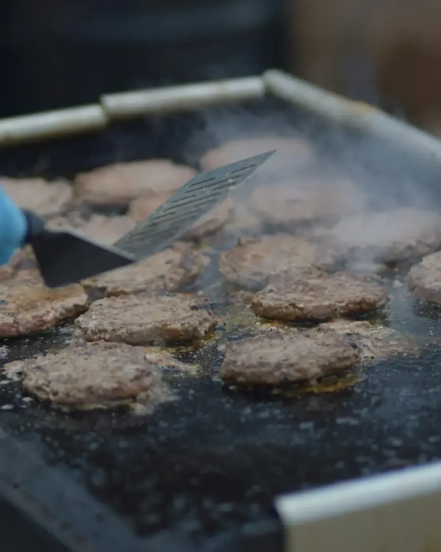 A cook pressing balls of beef flat on a griddle with a steel smasher