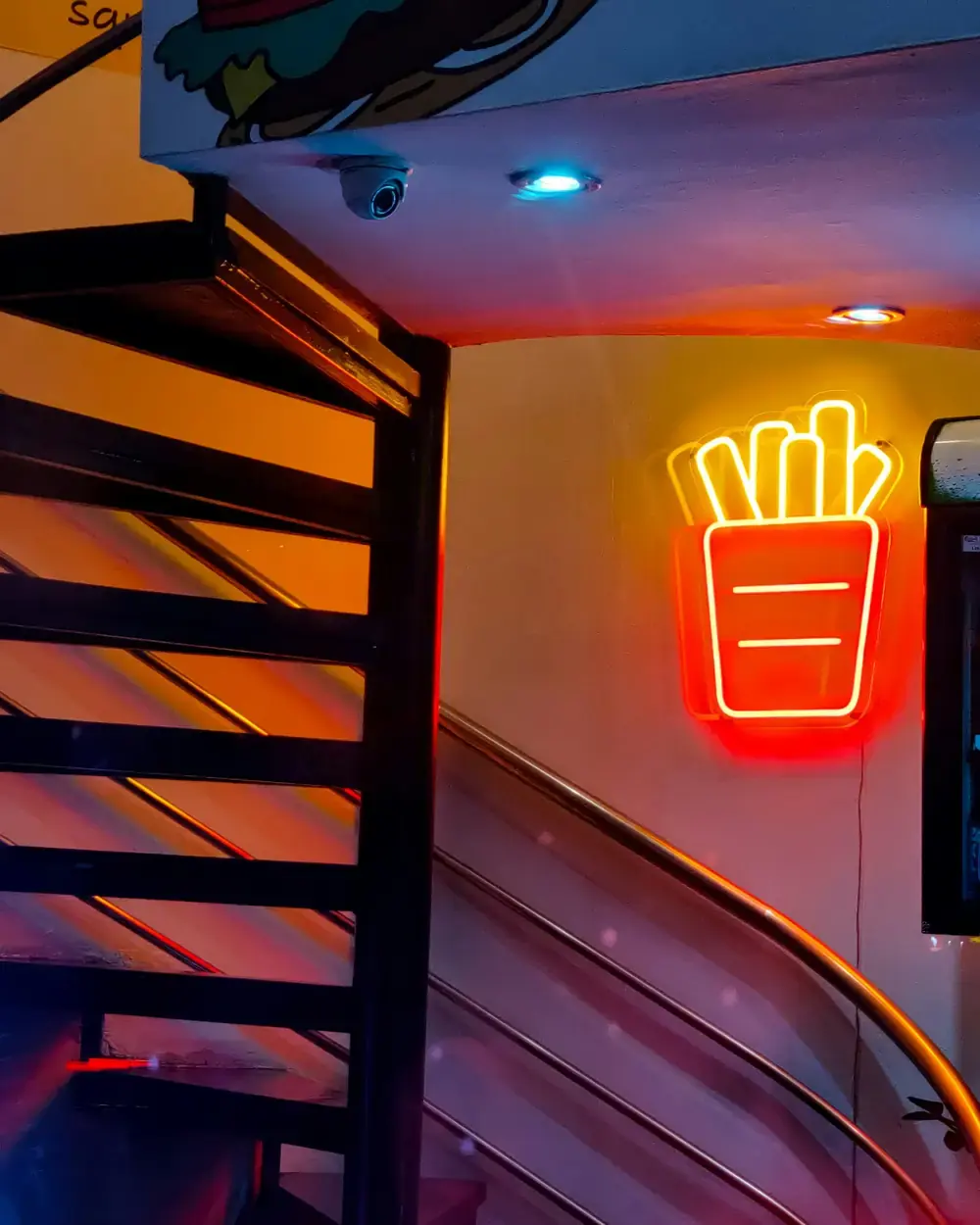 A neon fries sign glowing on the stairway wall